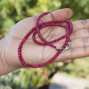 Op de afbeelding: Een ketting van robijnrode kralen geregen aan een zilveren ketting. De ketting wordt getoond op een hand.