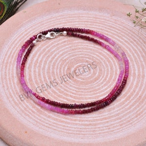 May include: A double strand necklace made of pink and red gemstone beads. The necklace has a silver clasp.