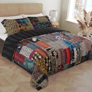 May include: A bed with a patchwork quilt and matching pillow shams. The quilt features a variety of colorful fabric patches in shades of red, blue, yellow, and black. The bed has a neutral-toned headboard and white sheets.