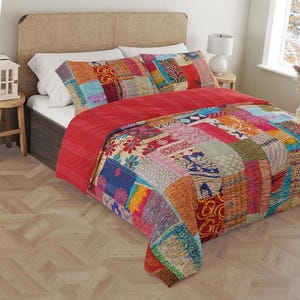 Peut inclure: Une courtepointe patchwork colorée avec un dos rouge et une variété de motifs floraux et géométriques. La courtepointe est sur un lit avec des taies d'oreiller blanches et à motifs.