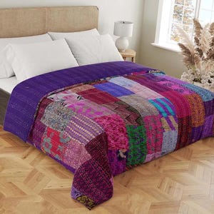 May include: A patchwork quilt in shades of purple, pink, and red covers a bed. The quilt features a variety of patterned fabrics, creating a vibrant and textured appearance. The bed is made up with white pillows and a purple bedspread.