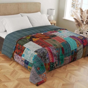 Könnte beinhalten: Eine Patchwork-Quilt auf einem Bett. Der Quilt zeigt eine Vielzahl von bunten Stoffquadraten in Rot-, Blau-, Grün- und Lilatönen. Das Bett hat weiße Kissen und ein neutrales Kopfteil. Der Quilt ist etwa 203 cm breit und 229 cm lang.