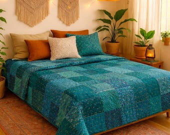May include: A bed featuring a teal patchwork quilt with intricate stitching, layered with two solid orange pillows, one beige pillow, and one white textured pillow. The bed is set against a wall with two macrame wall hangings and string lights.