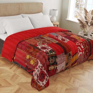 May include: A red patchwork quilt on a bed. The quilt features a variety of patterned fabric squares in shades of red, orange, and yellow. The bed has white pillows and a neutral headboard. The quilt is a decorative bedding item.