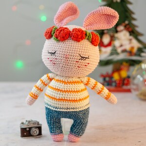 May include: A crocheted pink bunny wearing a flower crown and a striped orange and white sweater with blue jeans.