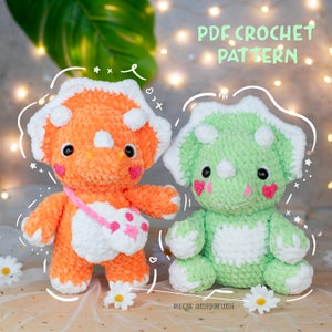 Pode incluir: Dois brinquedos de triceratops amigurumi de crochê. Um é laranja e o outro é verde. Ambos têm detalhes brancos e rostos fofinhos. Padrão de crochê PDF.