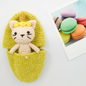 May include: A crocheted yellow and green sleeping bag with a crocheted cat wearing a yellow flower crown inside.