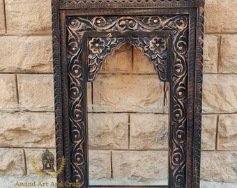 May include: A rectangular dark brown wooden wall frame featuring intricate hand-carved floral and scroll patterns. The frame has an arched inner opening and a decorative top panel. The text Anand Art And Craft The Unique Handicraft Furniture is visible in the lower left corner.