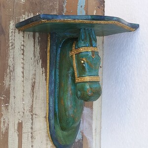 May include: A wall-mounted shelf featuring a sculpted horse head support. The horse is finished in a distressed teal and green patina with gold-toned trim along the bridle and the edges of the shelf. The shelf has a flat top surface.