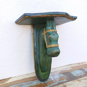 May include: A wall-mounted shelf featuring a sculpted horse head support. The piece is finished in a dark teal and green patina with gold-coloured trim detailing along the edges of the shelf and the horse's bridle and harness.
