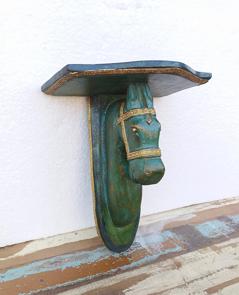 May include: A wall-mounted shelf featuring a sculpted horse head support. The piece is finished in a dark teal and green patina with gold-coloured trim detailing along the edges of the shelf and the horse's bridle and harness.