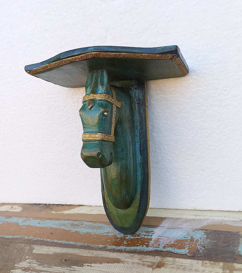 May include: A wall-mounted shelf featuring a horse head sculpture as the support bracket. The piece is finished in a distressed teal and green patina with ornate gold-coloured trim detailing along the edges of the shelf and the horse's bridle.