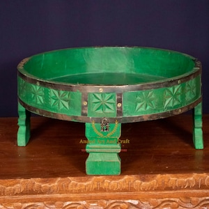 May include: A round green wooden tray with four short legs, featuring carved star patterns along the exterior rim. The tray is accented with dark metal bands and small brass-colored rivets. The text Anand Art And Craft is visible on the front leg.