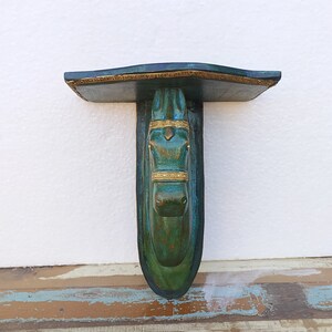 May include: A wall-mounted shelf featuring a sculpted horse head support. The piece is finished in a deep teal and green patina with gold-coloured accents on the horse's bridle and the shelf's front edge. The design includes a flat top surface.