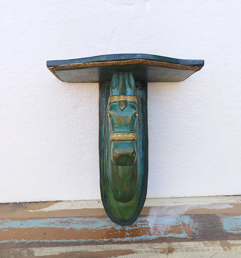 May include: A wall-mounted shelf featuring a sculpted horse head support. The piece is finished in a deep teal and green patina with gold-coloured accents on the horse's bridle and the shelf's front edge. The design includes a flat top surface.