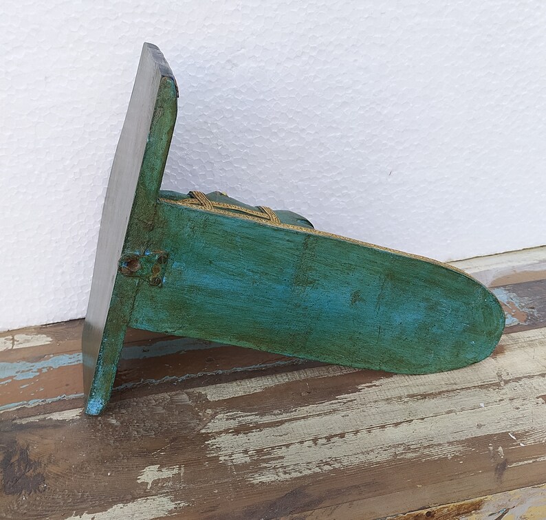 May include: A teal-coloured wooden wall shelf with a distressed finish and a flat, rectangular back panel. The shelf features a rounded front edge and is accented with a thin, gold-coloured decorative trim along the top perimeter of the horizontal surface.