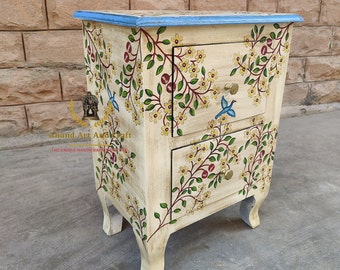 May include: A cream-colored wooden bedside table with two drawers, featuring hand-painted floral vines, green leaves, red berries, and blue birds. The top edge is painted blue, and each drawer has a single gold-toned hexagonal knob handle.