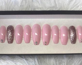 Uñas postizas pintadas a mano en color rosa con detalles de purpurina y diamantes de imitación.