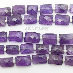 May include: Rows of faceted amethyst gemstone beads. The rectangular beads are a deep purple color and strung on a white string. The image includes the text "Jaipur Gems Gallery".