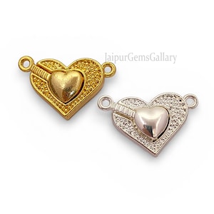 May include: Two heart-shaped jewelry clasps. One is gold-toned with a textured border and a smaller heart in the center. The other is silver-toned with a similar design. Both have loops for attachment and are on a white background.