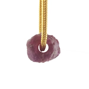 May include: A pink gemstone pendant on a gold chain. The gemstone is rough and has a natural, irregular shape.