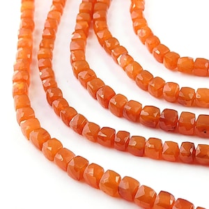 May include: A strand of orange carnelian beads, each bead is faceted and has a square shape. The beads are strung on a silver wire.