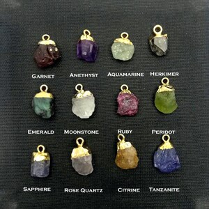 May include: Assortment of 12 gemstone pendants with gold settings. Each pendant features a different gemstone, including garnet, amethyst, aquamarine, herkimer, emerald, moonstone, ruby, peridot, sapphire, rose quartz, citrine, and tanzanite.