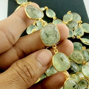 May include: A gold chain necklace with green gemstone beads. The beads are faceted and have a light green color with dark green inclusions. The chain is made of gold and has a delicate design.