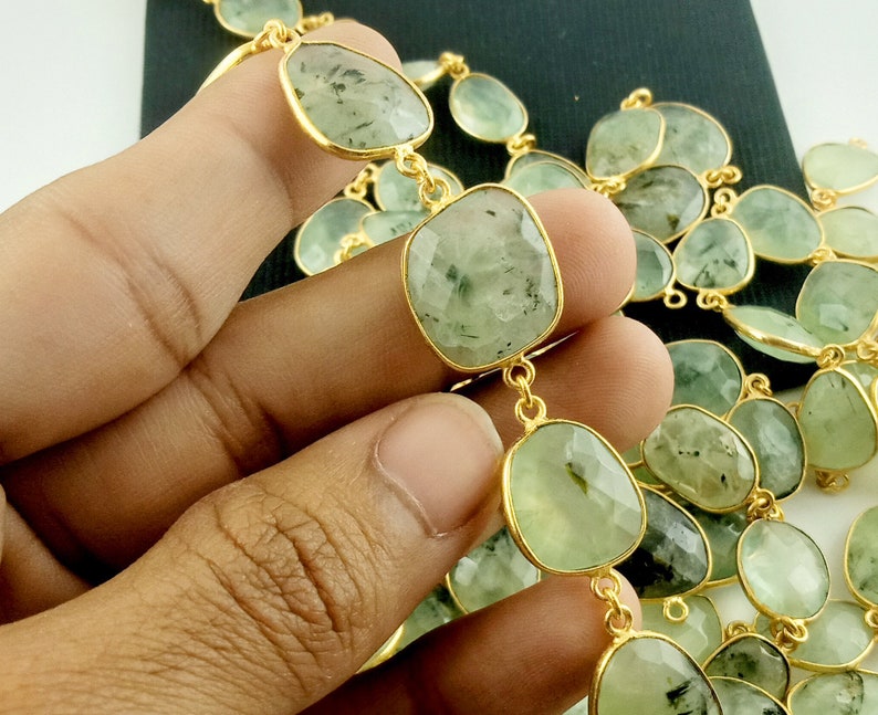 May include: A gold chain necklace with green gemstone beads. The beads are faceted and have a light green color with dark green inclusions. The chain is made of gold and has a delicate design.