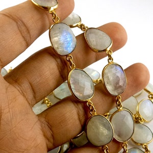 Peut inclure: Un collier en cha&icirc;ne dor&eacute;e avec des perles ovales en pierre de lune blanche. Le collier est pr&eacute;sent&eacute; sur une main.