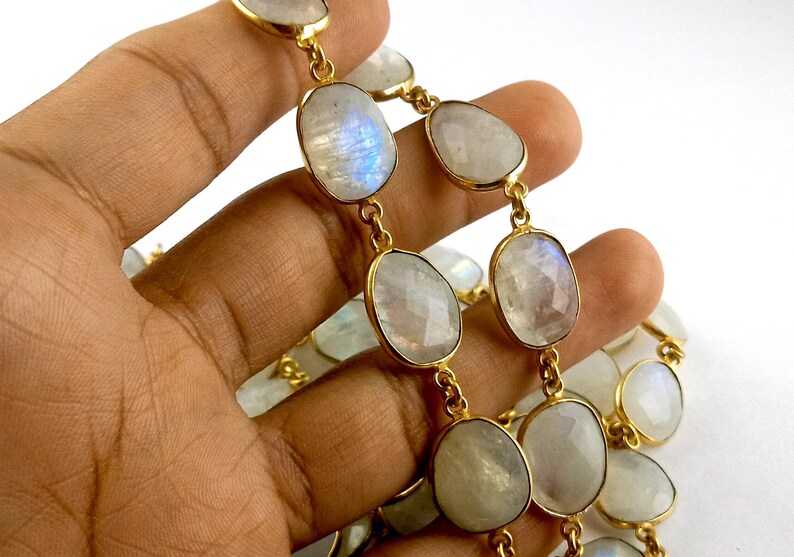 Peut inclure: Un collier en cha&icirc;ne dor&eacute;e avec des perles ovales en pierre de lune blanche. Le collier est pr&eacute;sent&eacute; sur une main.