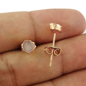 May include: A pair of rose gold stud earrings with a raw, natural crystal stone. The earrings have a simple, minimalist design.