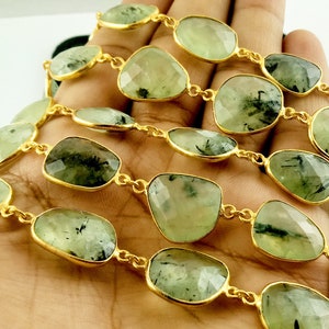 May include: A gold chain necklace with green and black gemstone beads. The beads are faceted and have a natural, organic look.