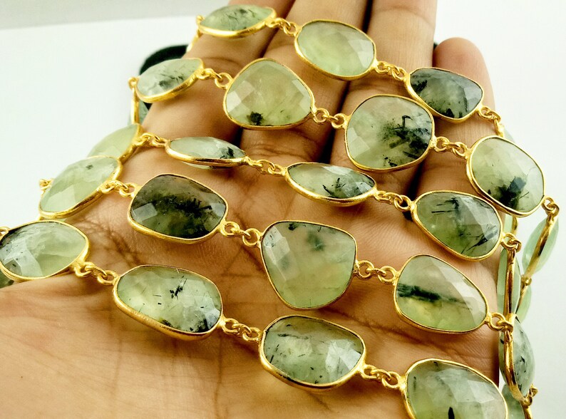 May include: A gold chain necklace with green and black gemstone beads. The beads are faceted and have a natural, organic look.