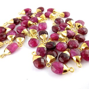 Op de afbeelding: Een groep roze edelsteen druppel hangers met vergulde springringen. De hangers zijn gefacetteerd en hebben een glanzende afwerking.