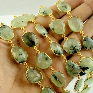 May include: A gold chain necklace with green gemstone beads. The beads are faceted and have a dark green, almost black, inclusion. The chain is made of small, round links.