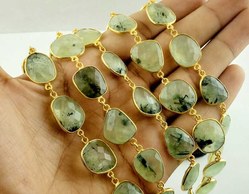 May include: A gold chain necklace with green gemstone beads. The beads are faceted and have a dark green, almost black, inclusion. The chain is made of small, round links.