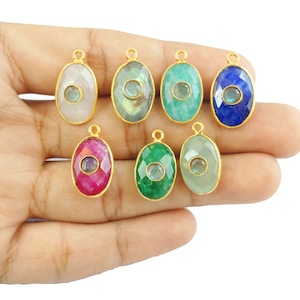 May include: Eight oval-shaped gemstone pendants with gold settings. Each pendant features a smaller round gemstone in the centre. The gemstones are in various colours, including white, grey, green, blue, and pink.