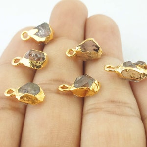 Pode incluir: Seis pingentes de cristal bruto banhados a ouro com um la&ccedil;o para prender em joias. Os cristais s&atilde;o transparentes com um leve tom cinza.