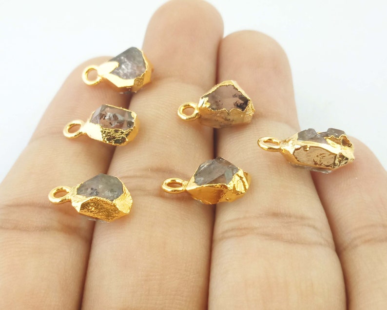 Pode incluir: Seis pingentes de cristal bruto banhados a ouro com um la&ccedil;o para prender em joias. Os cristais s&atilde;o transparentes com um leve tom cinza.