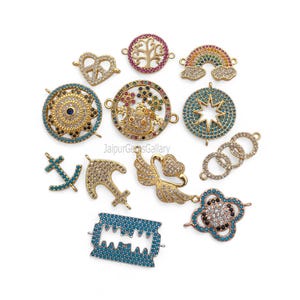 Può includere: Una collezione di ciondoli a forma di ciondolo dorati con accenti di zirconia cubica colorati. I disegni includono un segno di pace, un albero della vita, un arcobaleno, una stella, un'ancora, ali d'angelo e una lametta. I ciondoli sono per la creazione di gioielli.