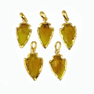May include: Five gold-plated arrowhead pendants with a translucent yellow-brown gemstone. The arrowheads are all the same size and shape, and they have a smooth, polished finish.