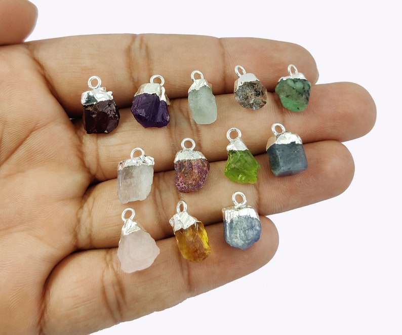 May include: Twelve raw gemstone pendants with silver bail settings. The gemstones are amethyst, aquamarine, ruby, emerald, sapphire, citrine, rose quartz, garnet, peridot, and clear quartz.