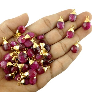 Pode incluir: Um lote a granel de 20 pingentes de pedra preciosa rosa em forma de lágrima com anéis de salto banhados a ouro. Os pingentes são facetados e têm um acabamento brilhante.