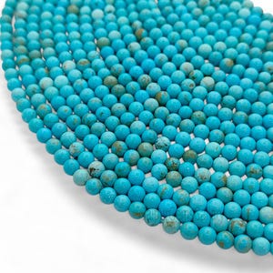 May include: A close-up of numerous turquoise beads, each spherical and displaying a polished finish. The beads, in shades of blue and brown, are tightly packed, forming a textured pattern. Suitable for crafting jewellery.