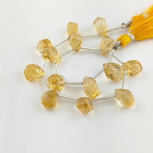 May include: A strand of golden yellow citrine gemstone beads, each bead is faceted and has a teardrop shape. The beads are strung on silver wire and have a tassel at the end.