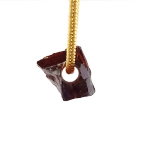 May include: A dark red gemstone pendant with a gold chain. The gemstone is irregularly shaped and has a hole drilled through it for the chain.