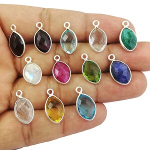 Puede incluir: Surtido de 12 colgantes de piedras preciosas con anilla de plata. Las piedras preciosas incluyen amatista, rubí, aguamarina, esmeralda, piedra lunar, citrino, zafiro y cuarzo transparente.