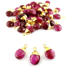 Op de afbeelding: Een groep van 25 roze edelsteen traan hangers met vergulde springringen. De hangers zijn gefacetteerd en hebben een glanzende afwerking. Drie hangers worden individueel getoond op een witte achtergrond.