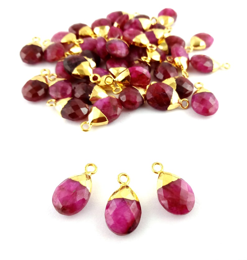 Op de afbeelding: Een groep van 25 roze edelsteen traan hangers met vergulde springringen. De hangers zijn gefacetteerd en hebben een glanzende afwerking. Drie hangers worden individueel getoond op een witte achtergrond.